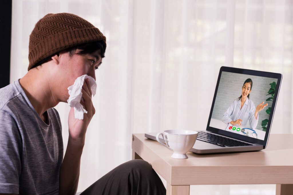 Young Asian male patient with sickness using laptop to video call conferencing with doctor at home. Medical .consultation via internet connection. Telecommunication Healthcare concept